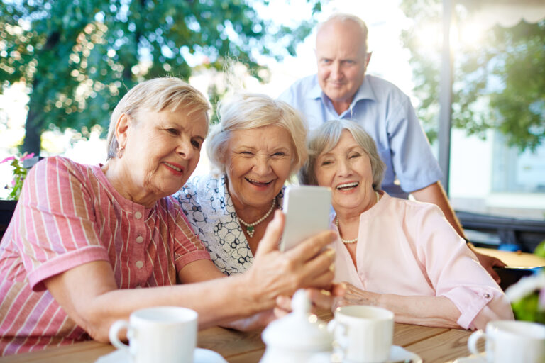 Four joyful childhood friends gathered together in outdoor cafe and taking picture of themselves